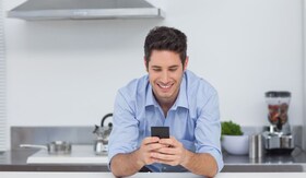 barbat tanar zambeste si se uita in telefonul mobil din maini intr-o bucatarie moderna